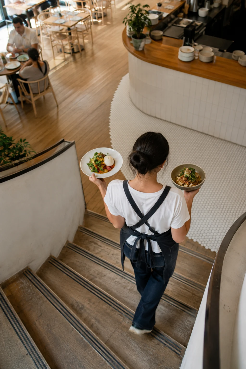 Overhead view of server carrying two appetizing plates across a curved restaurant stair landing.